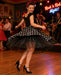 Frau im Rockabilly-Kleid wirbelt tanzend über die Tanzfläche, während eine Liveband bei einer Rock’n’Roll-Nacht spielt.